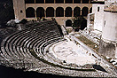 [image ALT: A Roman theater repaired with reinforced concrete, and with iron railings along the aisles up; surrounded by a church and a two-story cloister.]
